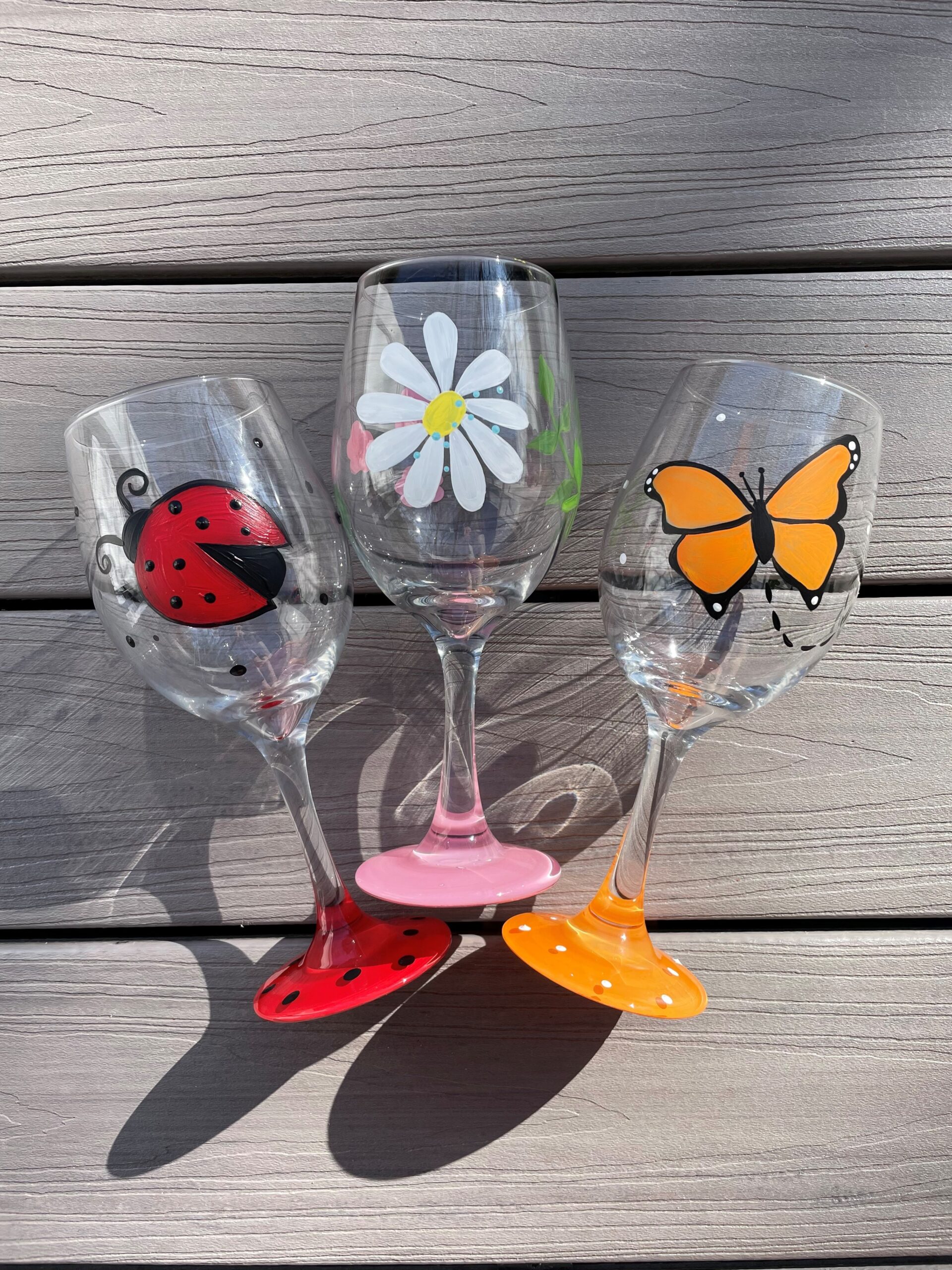 Colorful hand-painted wine glasses with ladybug, daisy, and butterfly designs for spring decor.