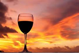 Elegant glass of red wine at sunset with vibrant sky.