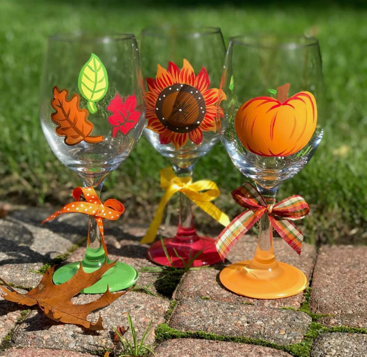 Decorative wine glasses with autumn-themed stickers and ribbons for Paint & Sip event.