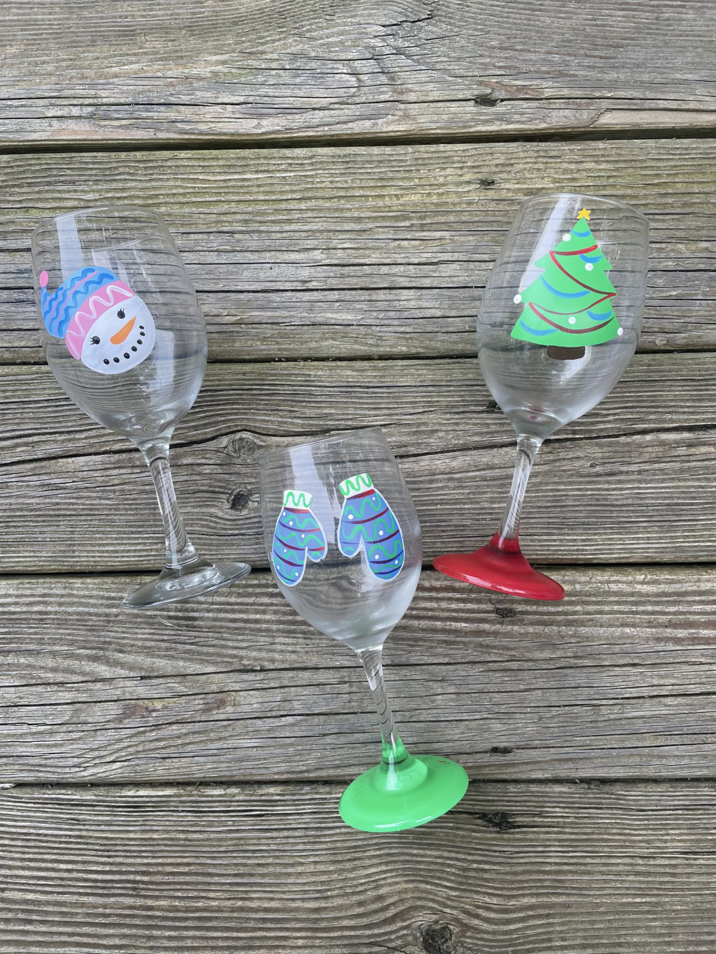 Festive wine glasses with Christmas-themed stickers on a wooden surface.